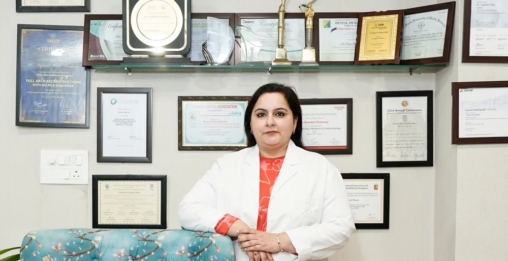 Dr. Supreet Kaur Sawhney in a white coat with professional certificates and awards displayed behind her